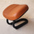 Brown saddle-like object on a black metal frame against a beige wall.